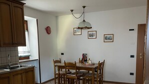 A kitchen with wooden cabinets, a dining table with chairs, a patterned rug, and a ceiling light fixture.