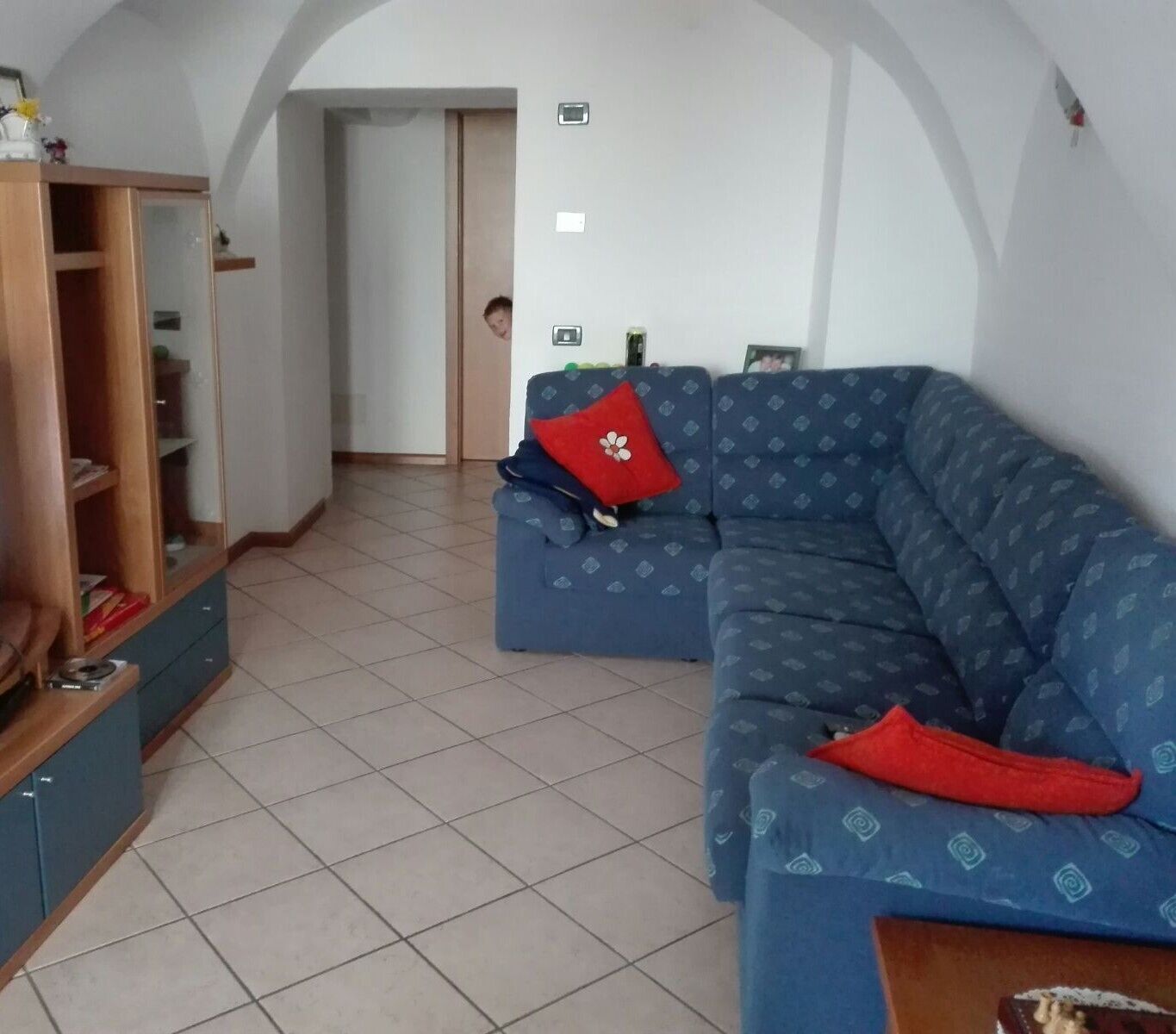 A living room with a blue sofa, a wooden cabinet, and a tiled floor.