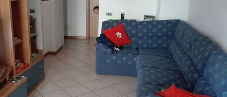 A living room with a blue sofa, a wooden cabinet, and a tiled floor.