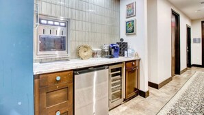 A modern kitchen with a stainless steel dishwasher, a built-in oven, and a microwave. There is a marble countertop with a decorative vase and a coffee maker. The kitchen is adjacent to a hallway with a patterned rug and a door. - Classic1 King Bed (Machu Picchu) (Dallas)