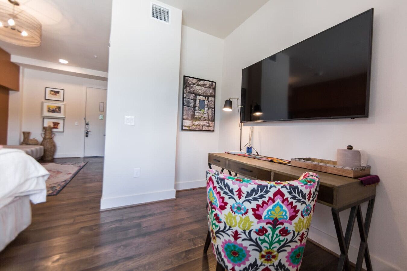 A bedroom with a bed, a desk, a chair, a TV, and a door.