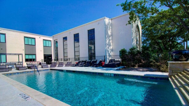 A swimming pool with lounge chairs and a building with large windows. - Classic1 King Bed (Machu Picchu) (Dallas)