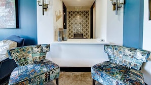 A room with two patterned chairs, a small table, and a decorative mirror with a geometric pattern. - Classic1 King Bed (Machu Picchu) (Dallas)