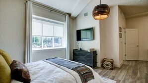 A bedroom with a large bed, a dresser, a television, and a window with curtains. - Angkor Wat- Room 102. Queen bed (Dallas)
