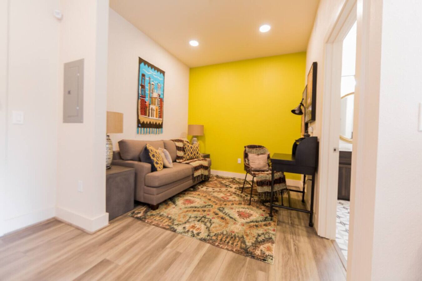 Un salon comprenant un canapé, un tapis à motifs, un coin repas avec une chaise et un mur d’accent jaune.