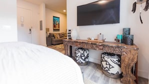 Une chambre d’hôtel comprenant un lit, un téléviseur fixé au mur, une console en bois agrémentée d’objets décoratifs et un pouf à motifs.