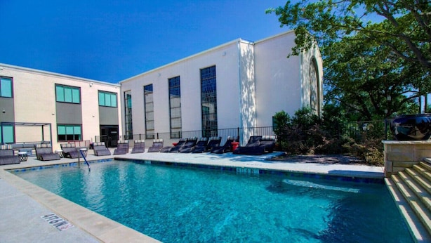 Une piscine avec des chaises longues et un bâtiment doté de grandes fenêtres.