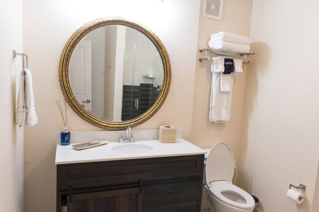 A bathroom with a round mirror, a sink, a toilet, and a towel rack with towels.