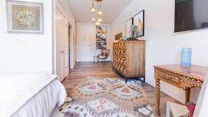 A hotel room with a bed, a wooden dresser, a small table, a rug, and a TV on the wall.