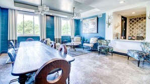 Une salle de conférence spacieuse, dotée d’une longue table et de nombreuses chaises, d’un coin salon avec des canapés et des fauteuils, et de grandes fenêtres équipées de rideaux.