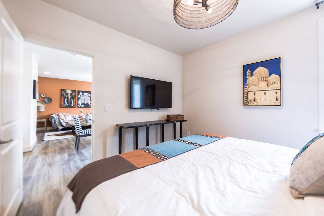 A bedroom with a bed, a TV, a painting, and a desk.