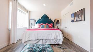 Un dormitorio con cama, cabecera, ventana, puerta y pared con un cuadro.