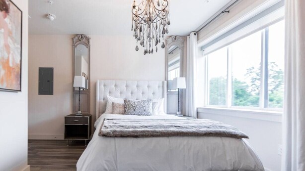 Une chambre moderne avec un grand lit, un lustre, une table de chevet et une fenêtre donnant sur un beau paysage.