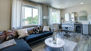 Un salon moderne avec un canapé bleu foncé, une table basse ronde et un coin repas comprenant une table et des chaises blanches.
