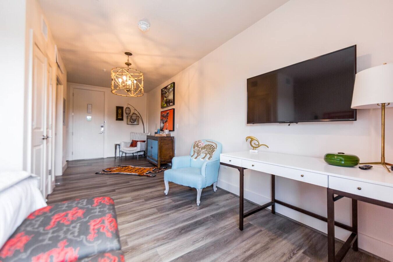 A hotel room with a bed, a desk, a chair, a TV, and a chandelier.