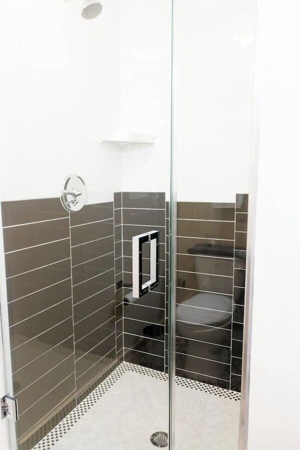 Zona de ducha con paredes de azulejos blancos, una puerta de cristal y un asiento negro.