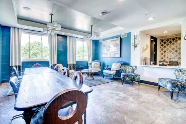 A spacious conference room with a long table and chairs, a seating area with sofas and armchairs, and a large window with curtains.