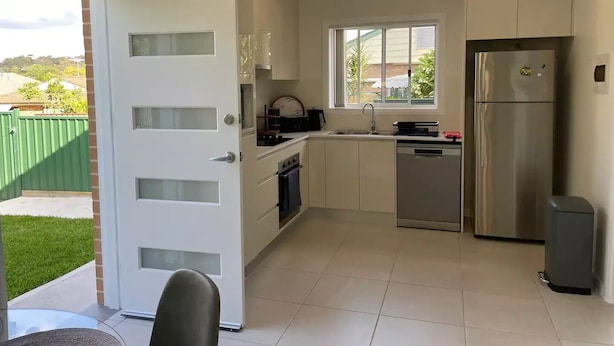 A modern kitchen with white cabinetry, a stainless steel refrigerator, and a window providing natural light. - Cosy Sunlit Home Away from Home

 (Baulkham Hills)