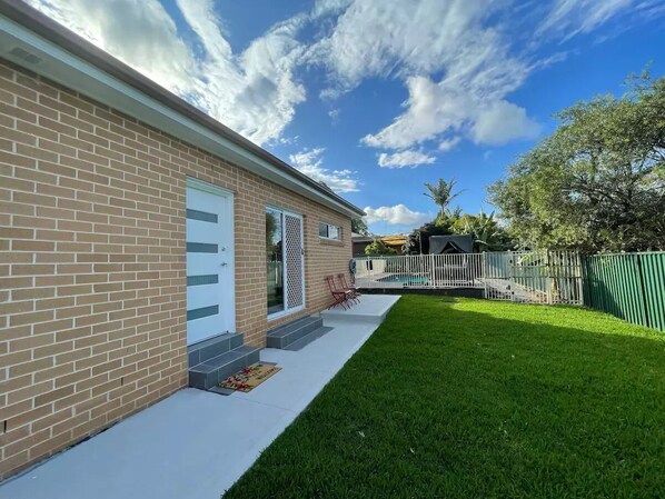 A brick building with a white door, a small porch, and a green lawn. - Cosy Sunlit Home Away from Home

 (Baulkham Hills)