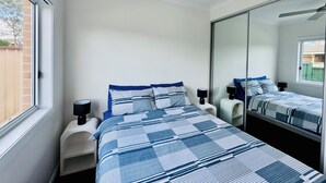 A bedroom with a large bed, a ceiling fan, a nightstand, and a mirror. - Cosy Sunlit Home Away from Home

 (Baulkham Hills)