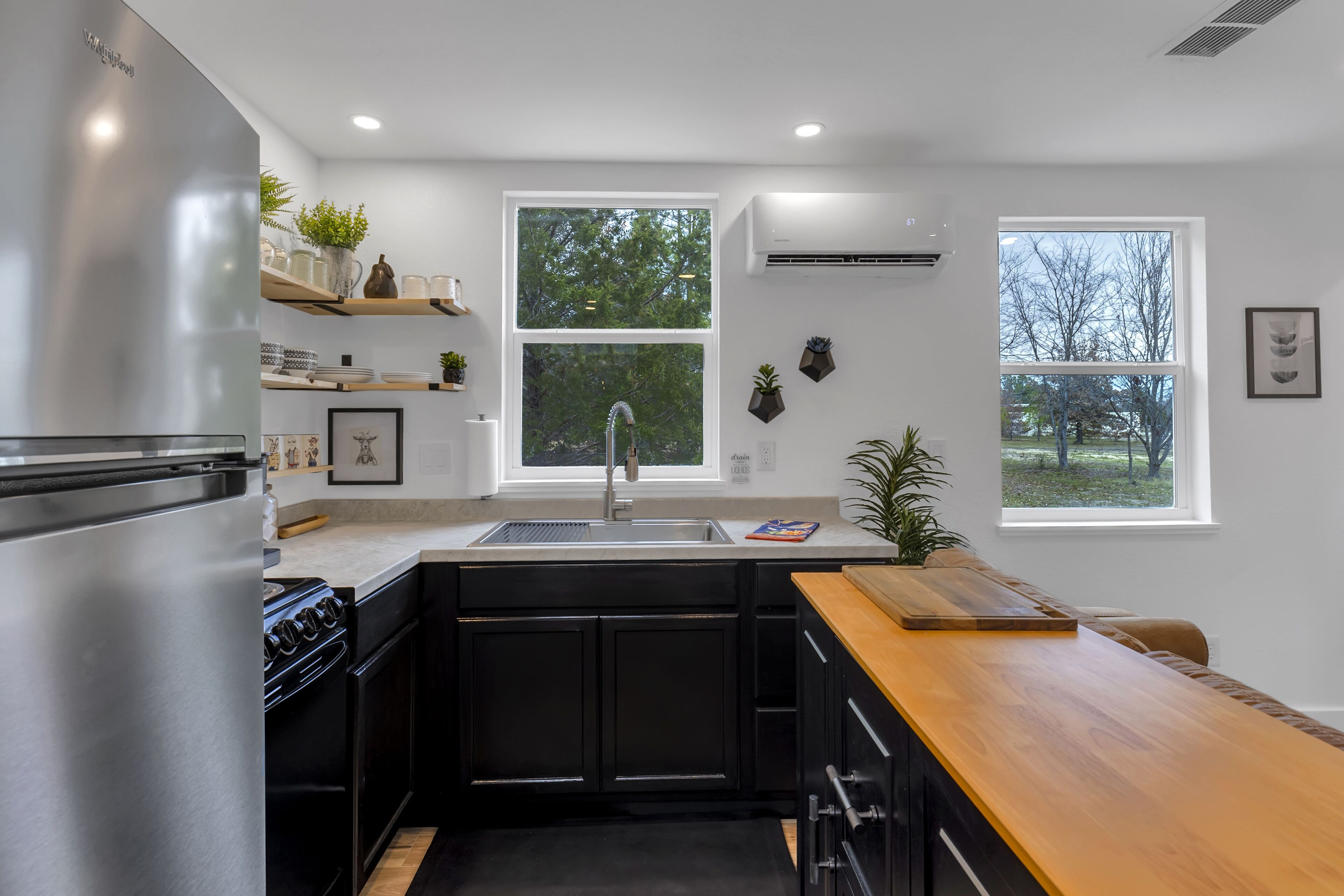 A modern kitchen with black cabinets, stainless steel appliances, and a wooden countertop.