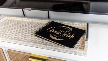A black guest book on a white tray with a heart-patterned mat, placed on a white cabinet with a gold handle.