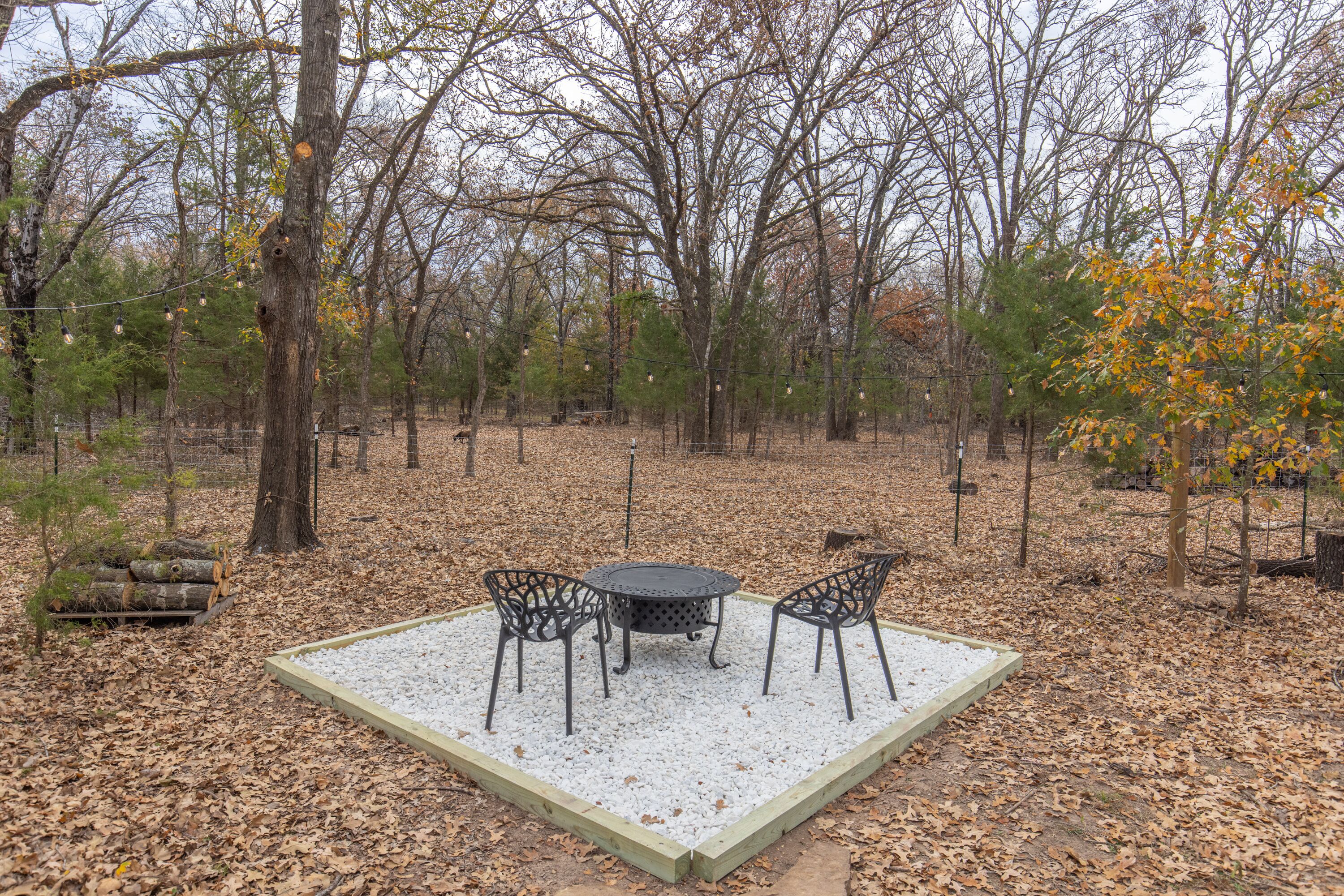 Een vierkant terras met een metalen tafel en stoelen, omgeven door een houten terras en een bebost achtergrond.