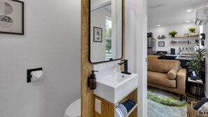 Un baño moderno con un lavamanos blanco, tocador de madera y un espejo.