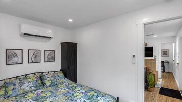 Een slaapkamer met een bloemenbedekking, een donkere garderobe en een wandairconditioner.