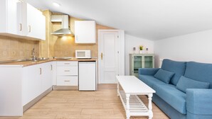 A compact kitchen with white cabinets, a microwave, and a stove. There is a blue sofa and a white table in the living area. - WintowinRentals Comfortable apartment in Málaga (Málaga)
