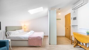 A bedroom with a bed, bedside table, and lamp; a wooden dining table with chairs; a wooden door; and an air conditioning unit on the wall. - WintowinRentals Comfortable apartment in Málaga (Málaga)