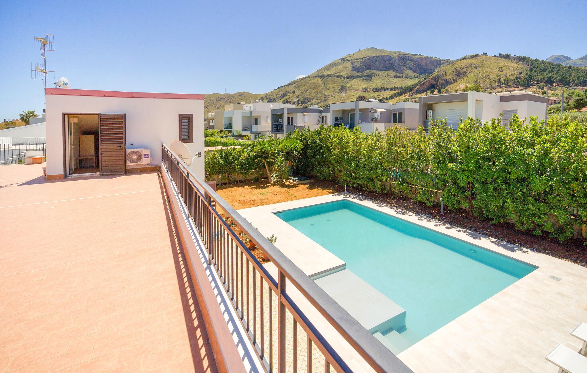 A modern residential complex with a swimming pool, a covered outdoor area, and a view of hills in the background.
