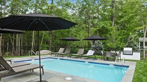 Ein Pool mit Liegestühlen und Sonnenschirmen, umgeben von einem Zaun und Bäumen.