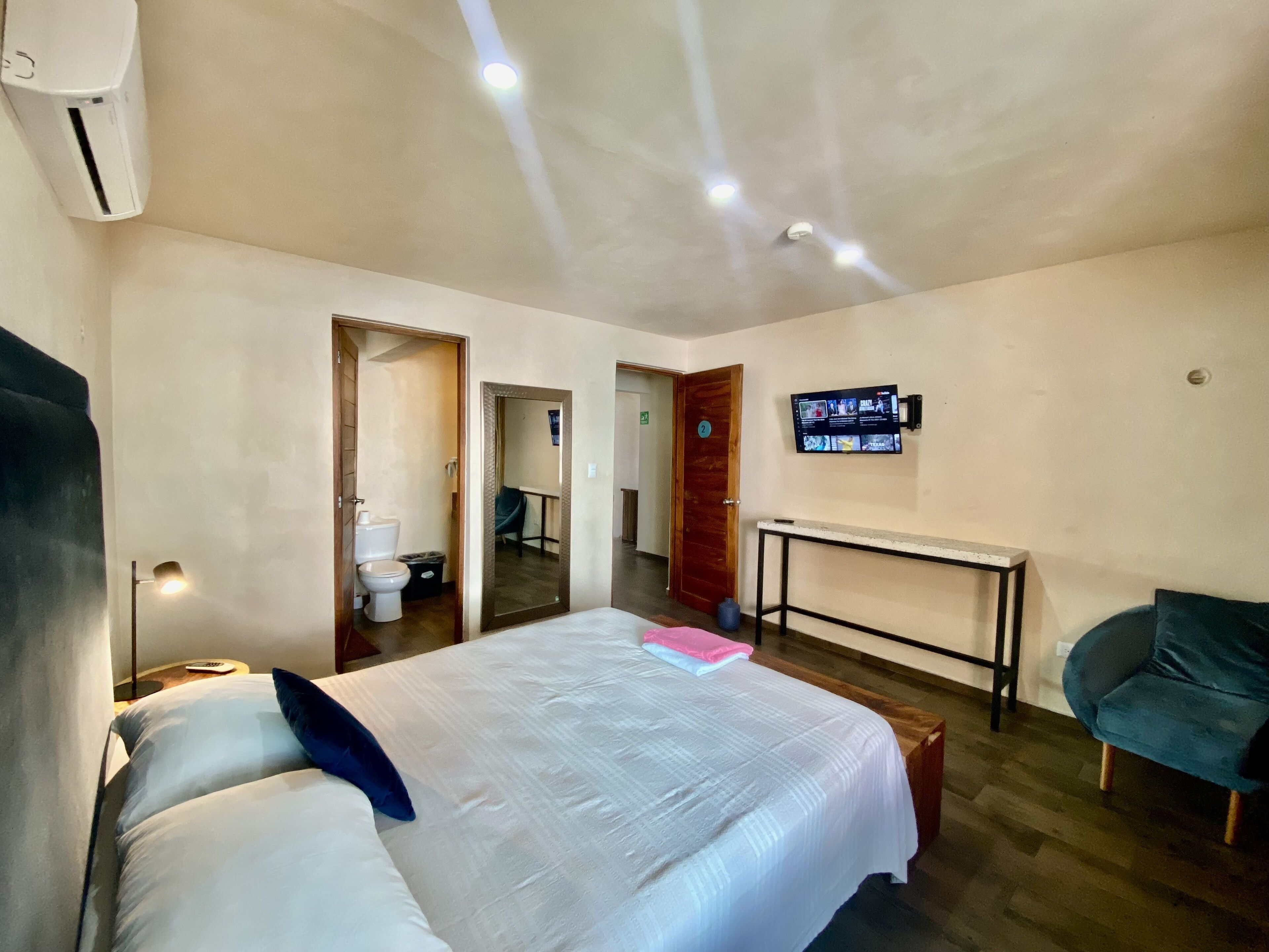 Een hotelkamer met een bed, nachtkastje, stoel en een aan de muur bevestigde televisie.