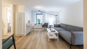 Ein modernes Wohnzimmer mit einem grauen Sofa, einem weißen Couchtisch, einer schwarzen Stehlampe und einem Schreibtisch mit Stuhl.