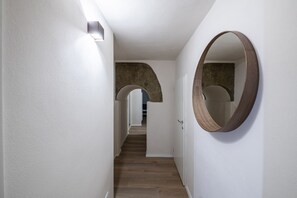 A hallway with white walls, a wooden floor, and a large mirror on the right.