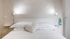 Ein ordentlich bezogenes Bett mit weißen Leinentüchern, einem herzförmigen Kopfkissen und zwei Nachttischlampen.