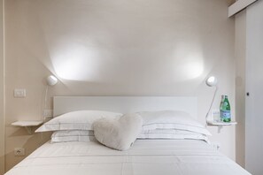 A neatly made bed with white linens, a heart-shaped pillow, and two bedside lamps.