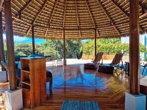 Une terrasse en bois à ciel ouvert, dotée d’un toit de chaume, de meubles en bois et d’un fauteuil suspendu.