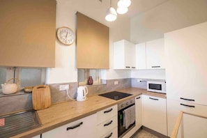 Eine moderne Küche mit Holzschränken, einer Mikrowelle, einem Backofen, einem Wasserkocher und einer Uhr an der Wand.