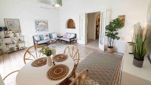 Un salón amplio con una mesa de comedor redonda, asientos cómodos y una planta grande.