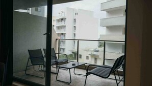 Een balkon met twee stoelen en een kleine tafel, met uitzicht op een woonwijk met meerhoogbouw.
