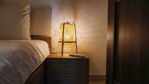 Een net opgemaakt bed met een witte deken en kussens, een nachtkastje met een lamp en een afstandsbediening erop.