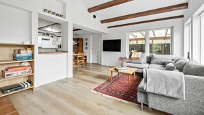 A spacious living room with a large grey sofa, wooden beams on the ceiling, and a TV mounted on the wall. - Beautiful home in Vejby with kitchen (Vejby)