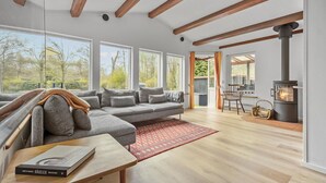 A modern living room with a large sectional sofa, a fireplace, and large windows offering a view of the outdoors. - Beautiful home in Vejby with kitchen (Vejby)