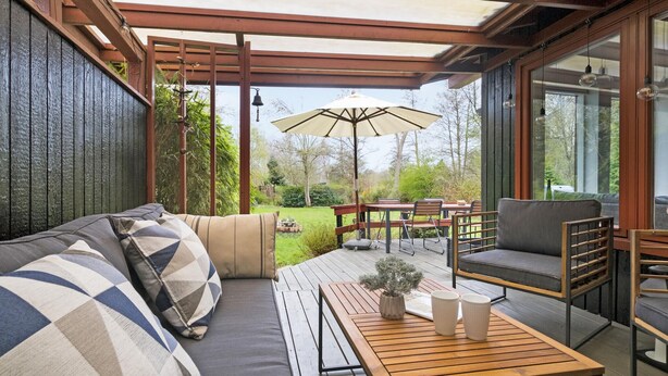 A covered outdoor seating area with a wooden bench, a sofa, and a table with a potted plant and two cups. - Beautiful home in Vejby with kitchen (Vejby)
