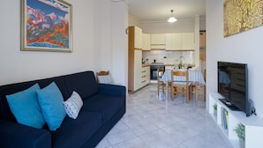 Ein Wohnzimmer mit einem dunkelblauen Sofa, einem Fernseher und einem Essbereich mit Tisch und Stühlen.