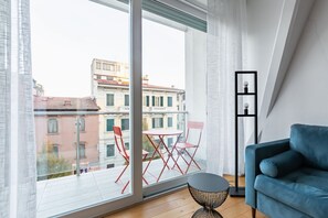 A modern apartment with a large window, a blue sofa, a small round table, and red chairs.