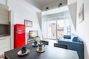 A modern kitchen with a red refrigerator, a dining table with a coffee pot, and a blue sofa. - GuestHost - Modern and bright 40 sqm apartment, located on the second floor of a modern building (with lift), for 4 people. The accommodation is located in a residential district, equipped with all the main services and well connected to the historic cen (Firenze)