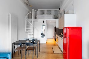 A modern kitchen with a red refrigerator, a dining area with a table and chairs, and a staircase leading to an upper level.
